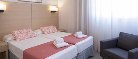 A hotel room with two beds, a grey armchair, and a painting on the wall.