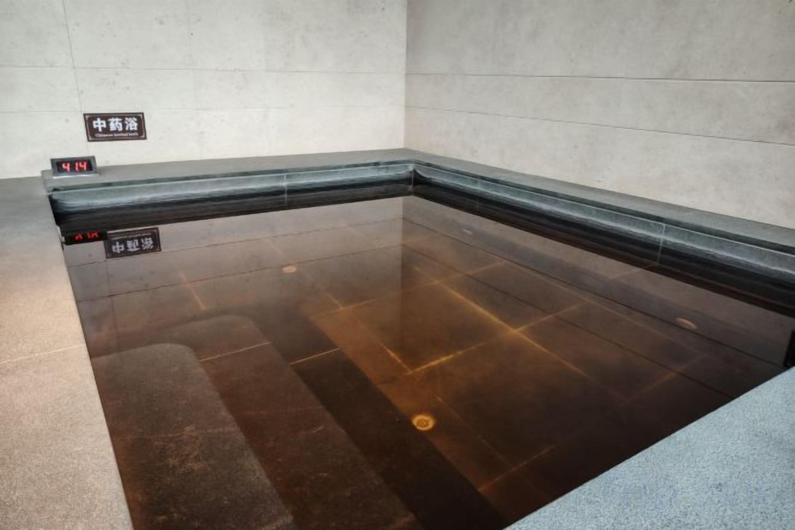 A swimming pool with a tiled floor and a dark border. There are signs on the wall indicating the pool's location.