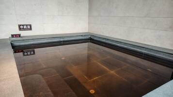 A swimming pool with a tiled floor and a dark border. There are signs on the wall indicating the pool's location.