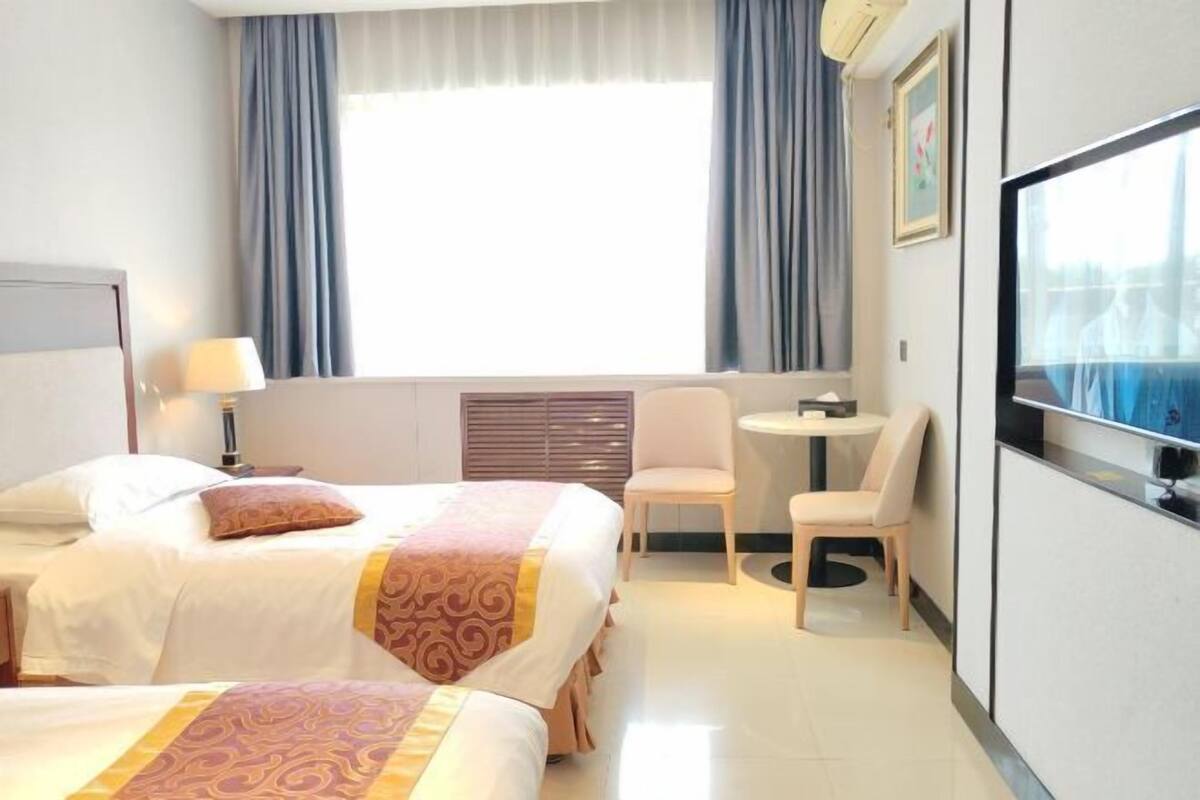 Une chambre d’hôtel avec deux lits, un bureau, une chaise, une télévision et une fenêtre avec des rideaux.