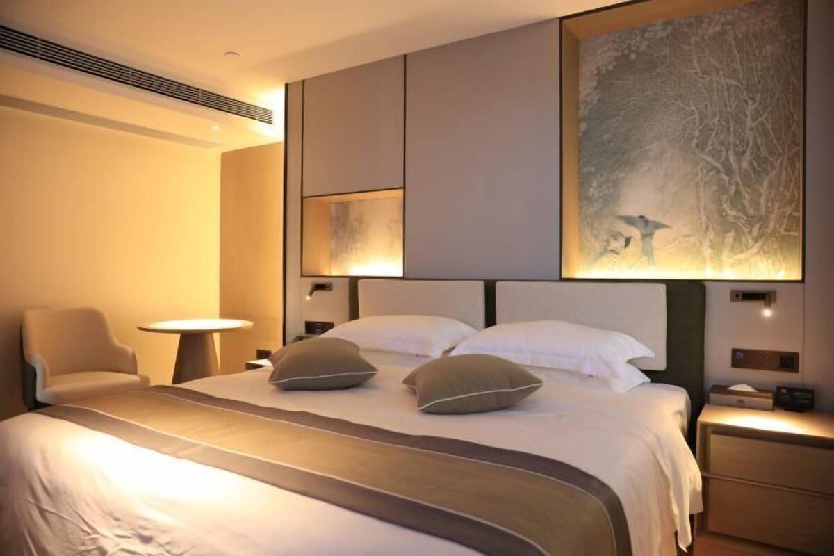 Une chambre d’hôtel avec un grand lit, deux tables de chevet, une chaise et une œuvre d’art accrochée au mur.