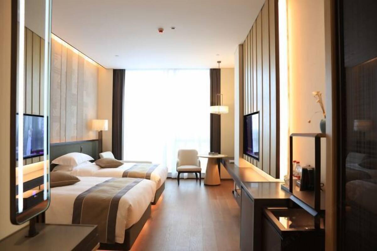 Une chambre d’hôtel avec deux lits, un bureau, une chaise, une télévision et une grande fenêtre.