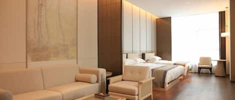 A modern hotel room with a large bed, a sofa, a chair, and a coffee table.