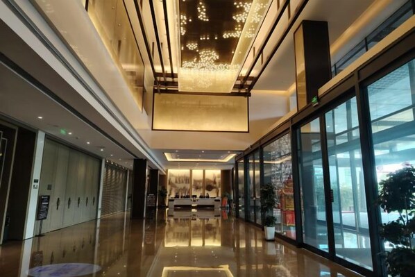 A modern hotel lobby with a reflective floor, large windows, and a central reception desk.