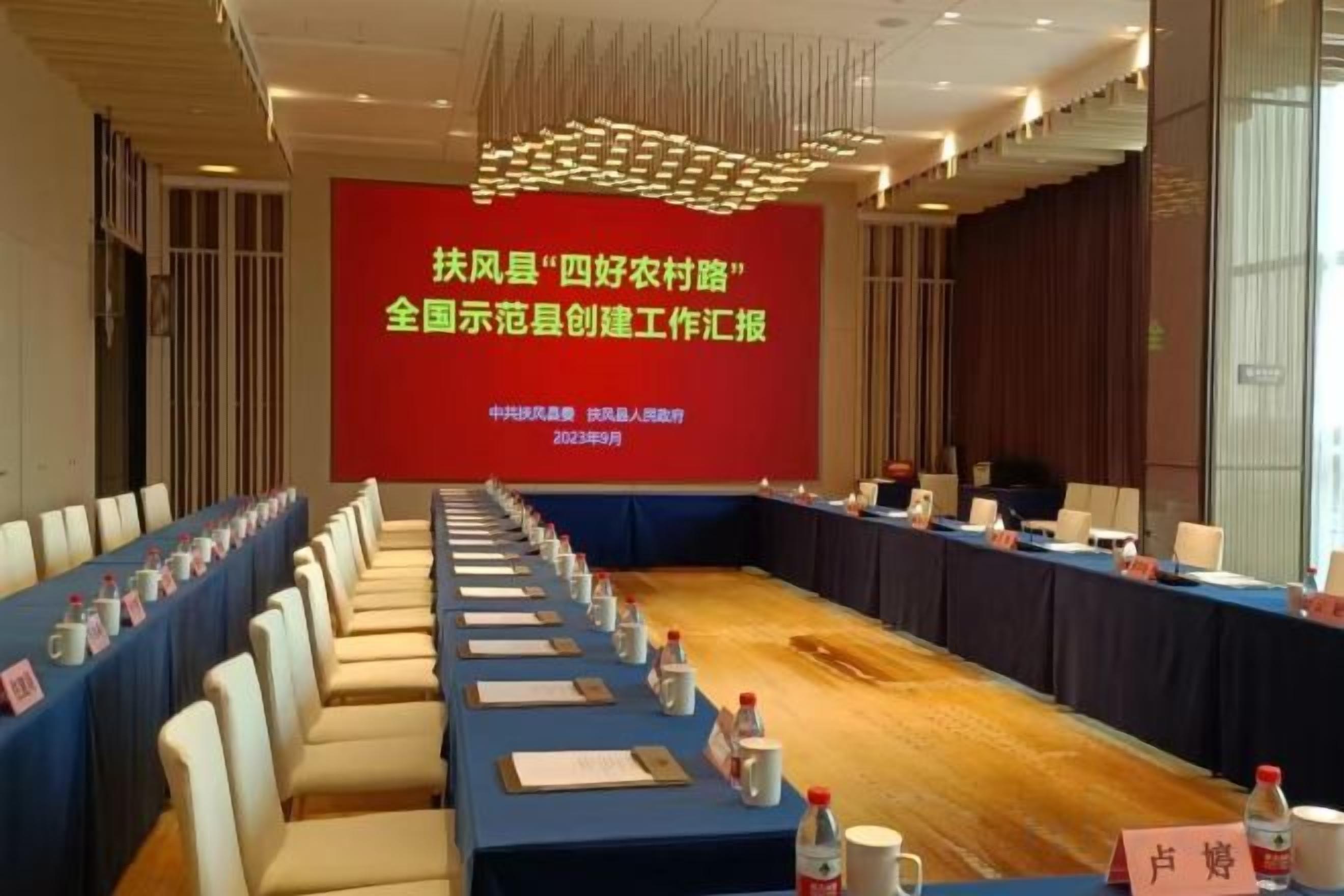 A conference room with a long table, chairs, and a presentation screen.
