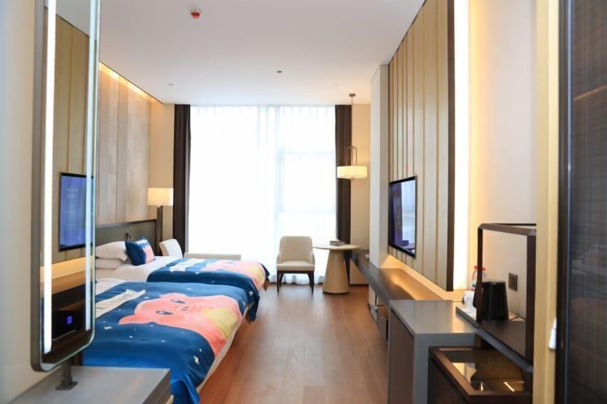 Een hotelkamer met een bed, bureau, stoel, televisie en een groot raam.