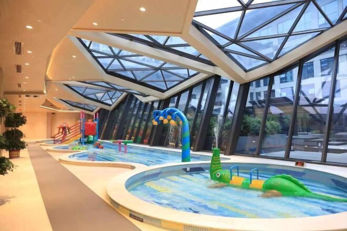 Une piscine intérieure dotée d’un toit en verre, d’un toboggan et d’un espace aménagé au bord du bassin avec des plantes.