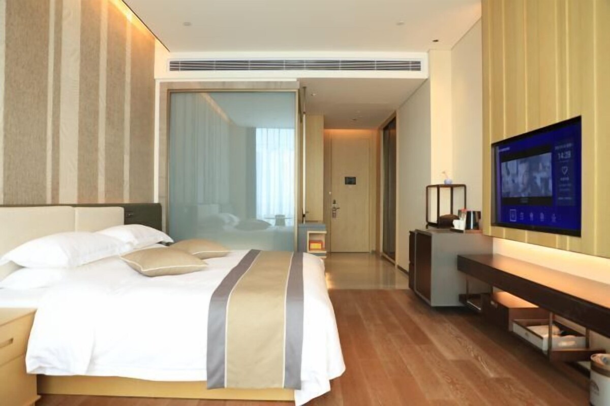 Een moderne hotelkamer met een bed, nachtkastje, televisie en uitzicht op de gang.