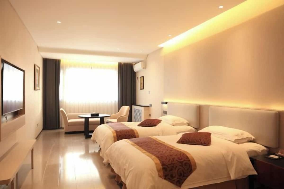 Une chambre d’hôtel avec deux lits, un bureau, une chaise et une grande fenêtre avec des rideaux.