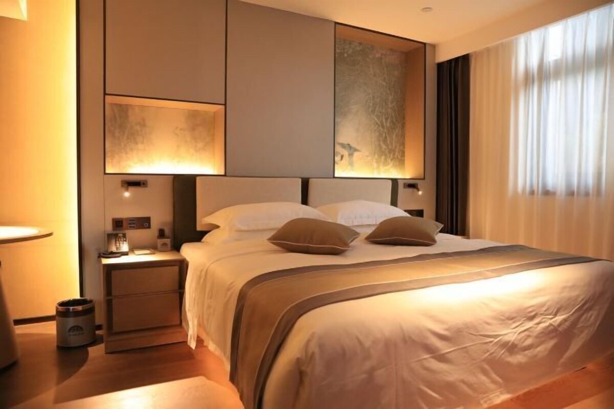 Een moderne hotelkamer met een groot bed, nachtkastjes en een kunstwerk aan de muur.