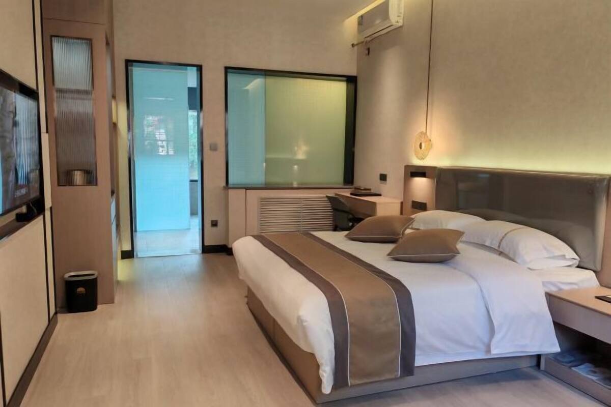 Une chambre d’hôtel moderne avec un grand lit, des tables de chevet, un bureau et une grande fenêtre.