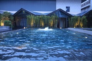 A swimming pool with a fountain, surrounded by modern buildings with large windows and a flat roof.