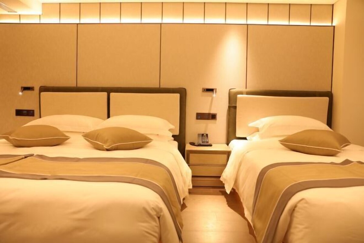 Een hotelkamer met twee bedden, elk met hoofdeinde en kussens. Tussen de bedden staat een nachtkastje met een lamp en telefoon.