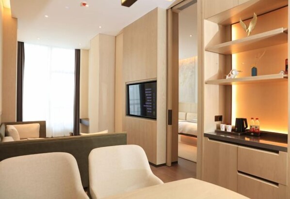 Een moderne hotelkamer met een flatscreen televisie aan de muur, een bank, een bed en een klein kitchenette met een koffiezetapparaat en flessen.