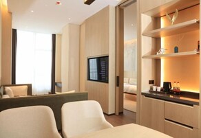 Una habitación de hotel moderna con una televisión de pantalla plana en la pared, un sofá, una cama y una pequeña zona de kitchenette con cafetera y botellas.