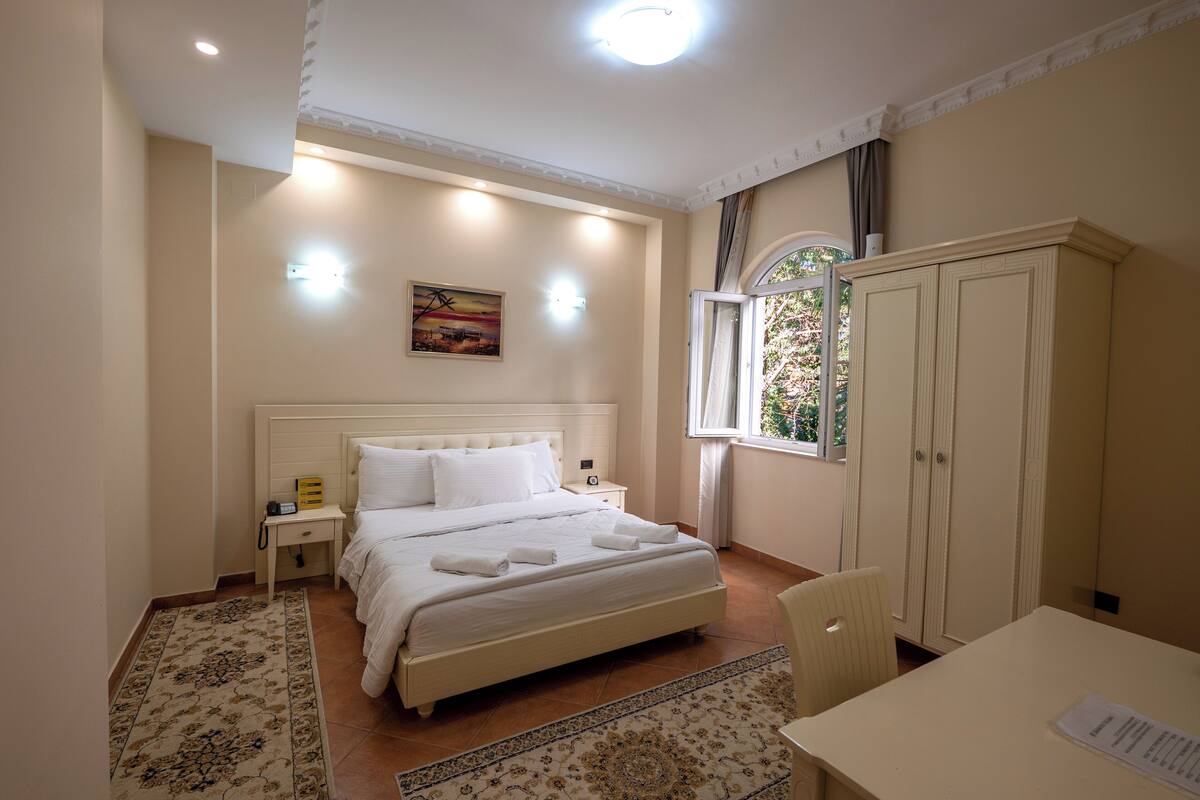 Ein Schlafzimmer mit Bett, Nachttisch, Kleiderschrank und einem Fenster mit Vorhängen.