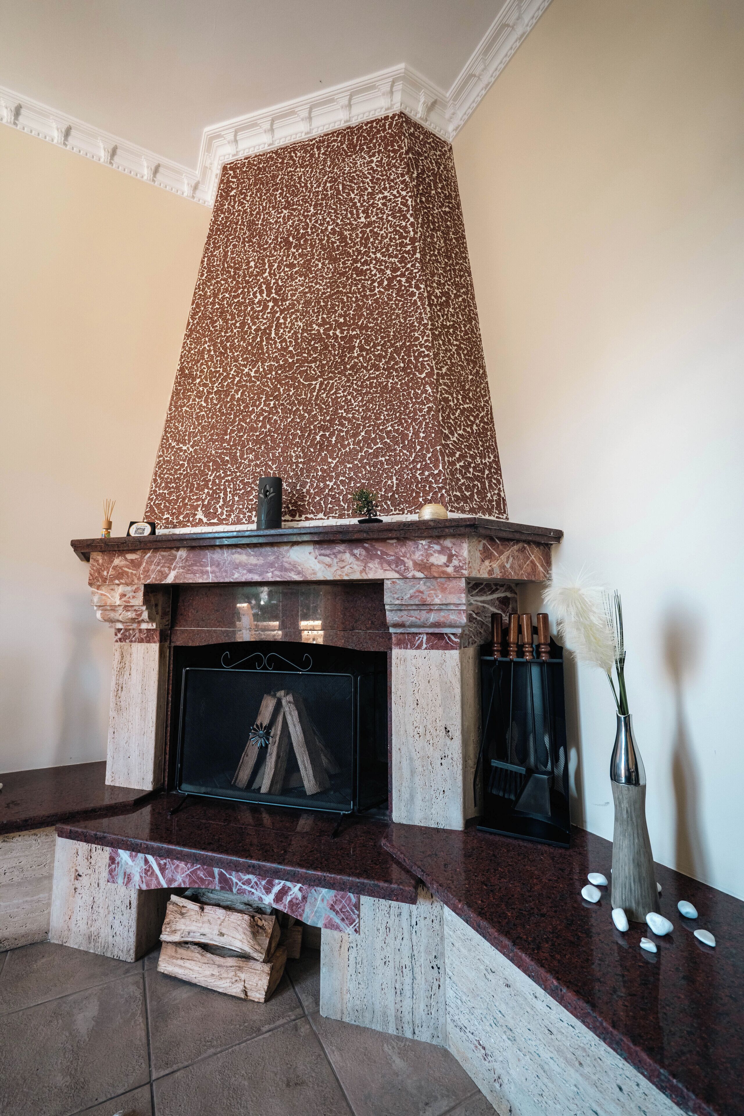 Een openhaard met een rustieke stenen schouw, een schoorsteenmantel met decoratieve voorwerpen, en een houtopslagplaats.