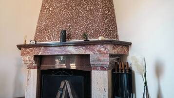 Een openhaard met een rustieke stenen schouw, een schoorsteenmantel met decoratieve voorwerpen, en een houtopslagplaats.
