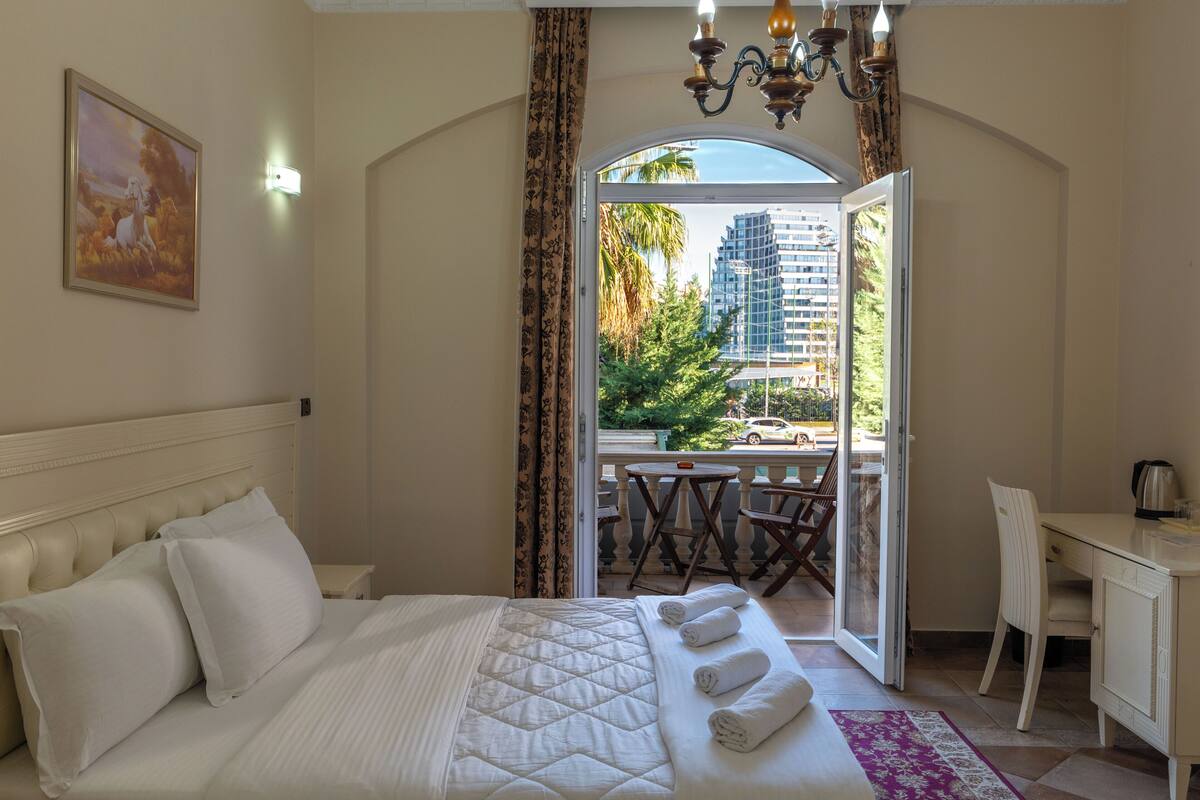 Ein Hotelzimmer mit Bett, Schreibtisch und einem Balkon mit Blick auf die Stadt.