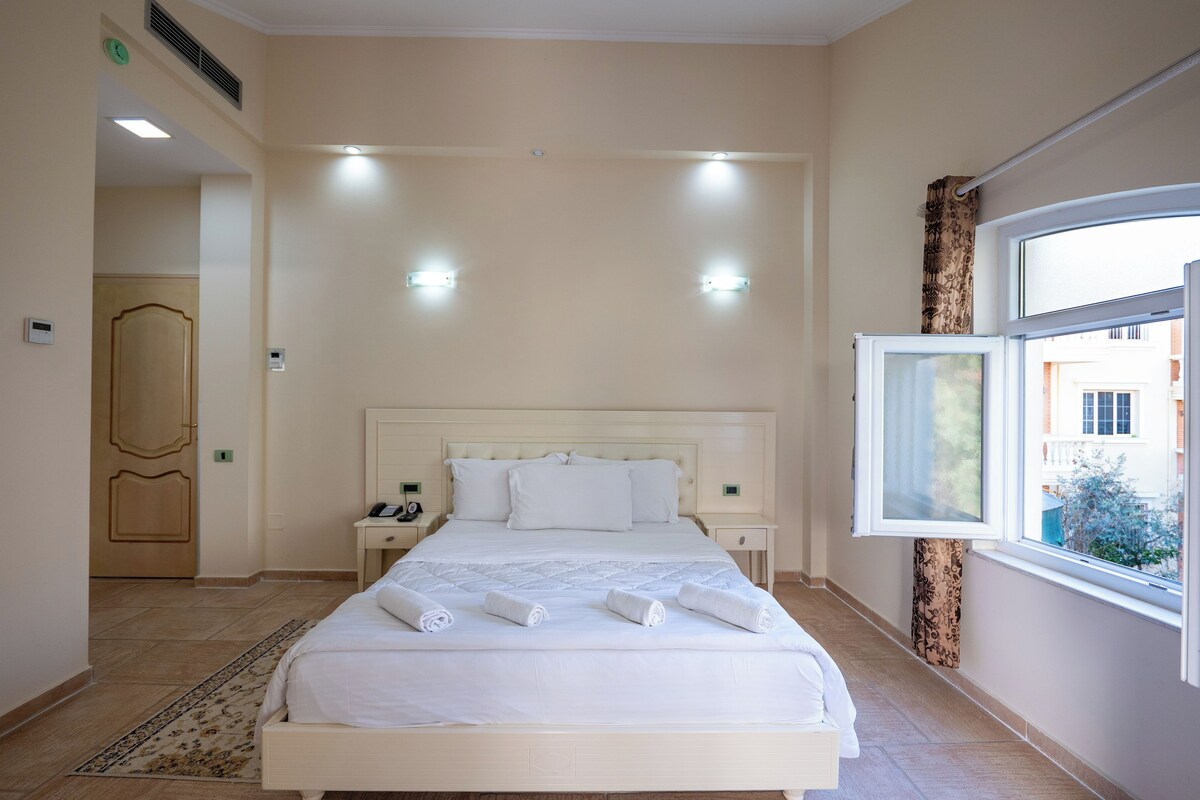 Habitación de hotel con una cama grande, mesitas de noche, una ventana con vistas y una puerta.