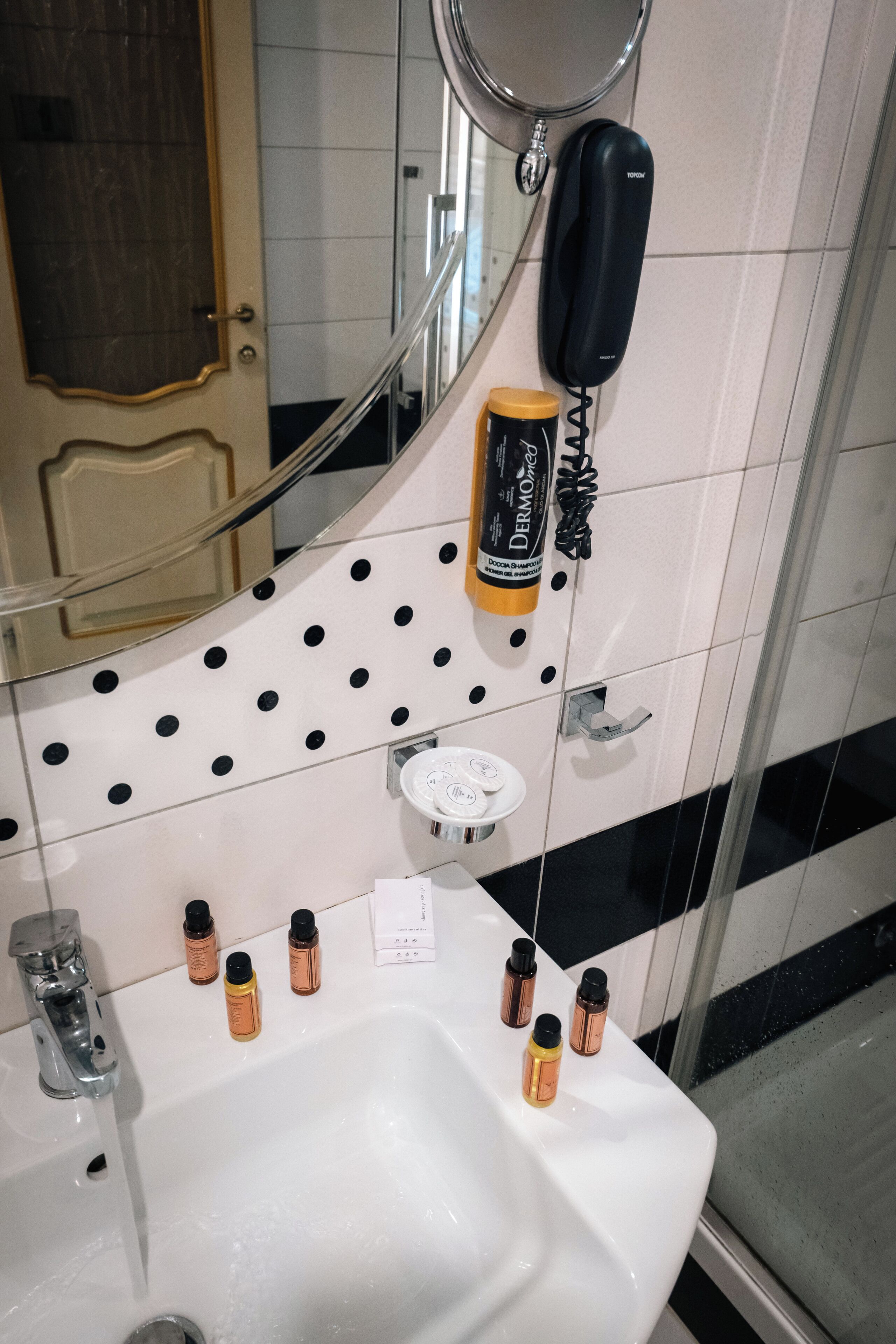 Een badkamer met een witte wastafel, een spiegel, een zwarte telefoon en diverse toiletartikelen.