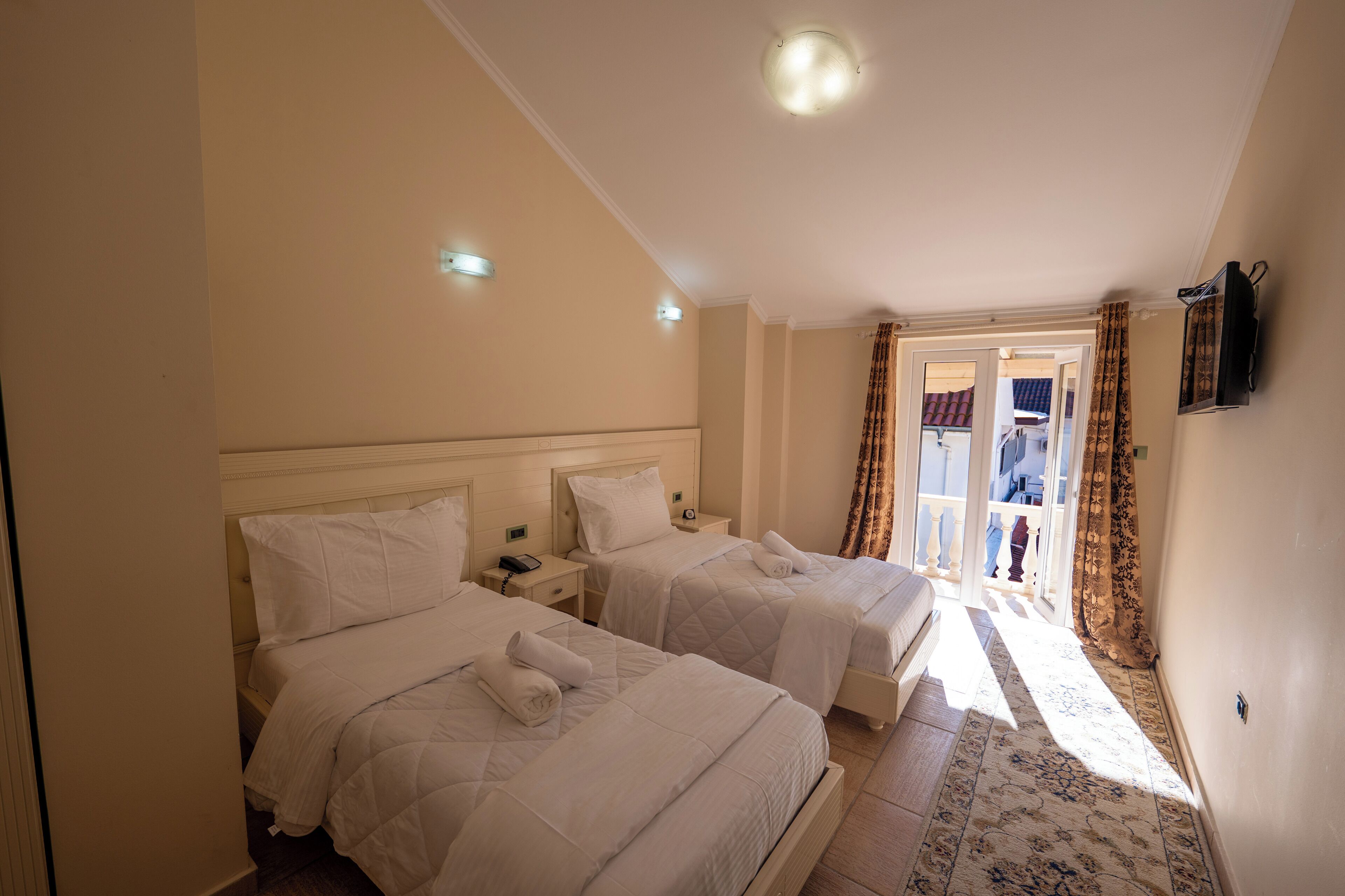 Habitación de hotel con dos camas, una mesita de noche pequeña con un teléfono y vistas al balcón exterior.