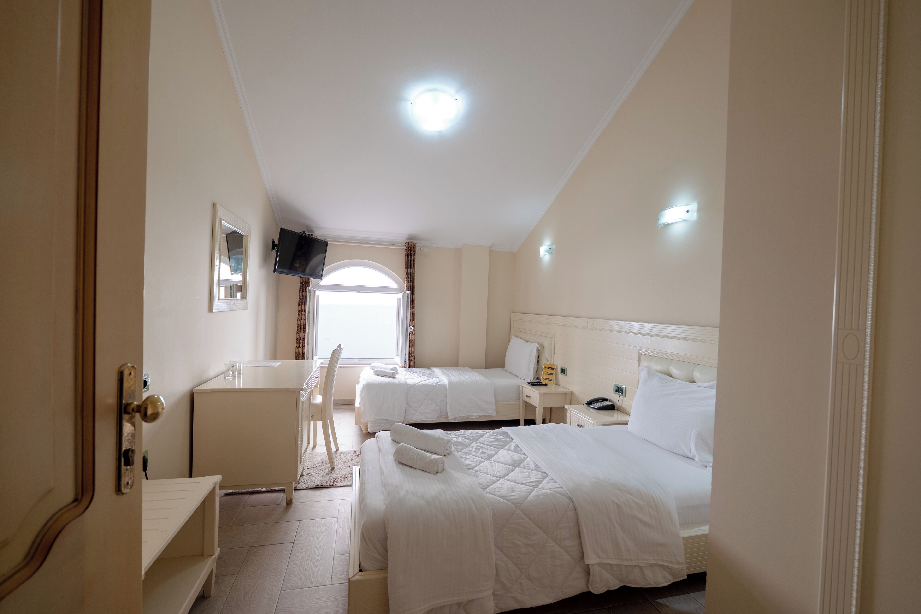 A hotel room with two beds, a desk, a chair, a TV, and a window with curtains.