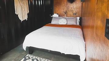 A bedroom with a bed, a patterned rug, a wall-mounted light fixture, and a ceiling fan.