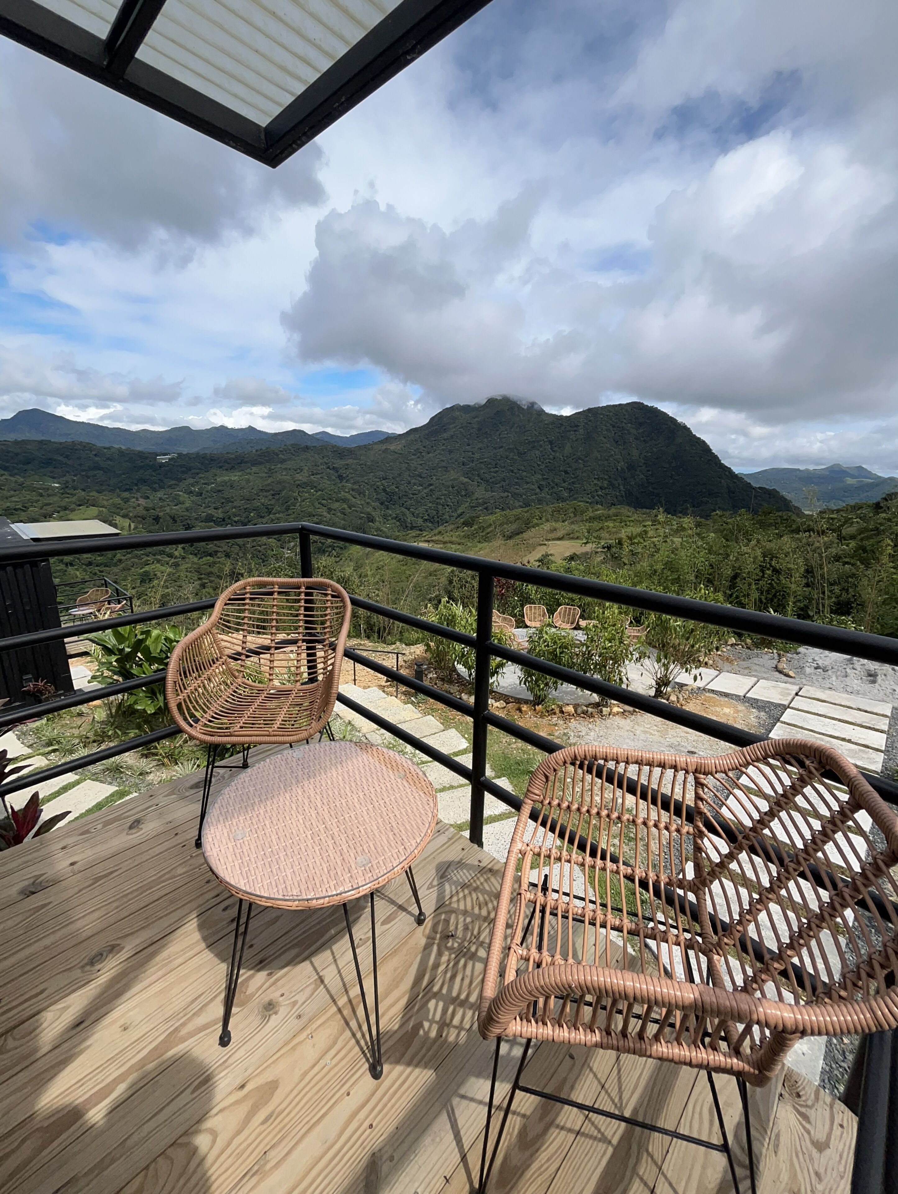 A wooden deck with wicker chairs and a table, overlooking a mountainous landscape.