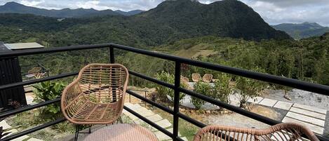 A wooden deck with wicker chairs and a table, overlooking a mountainous landscape.