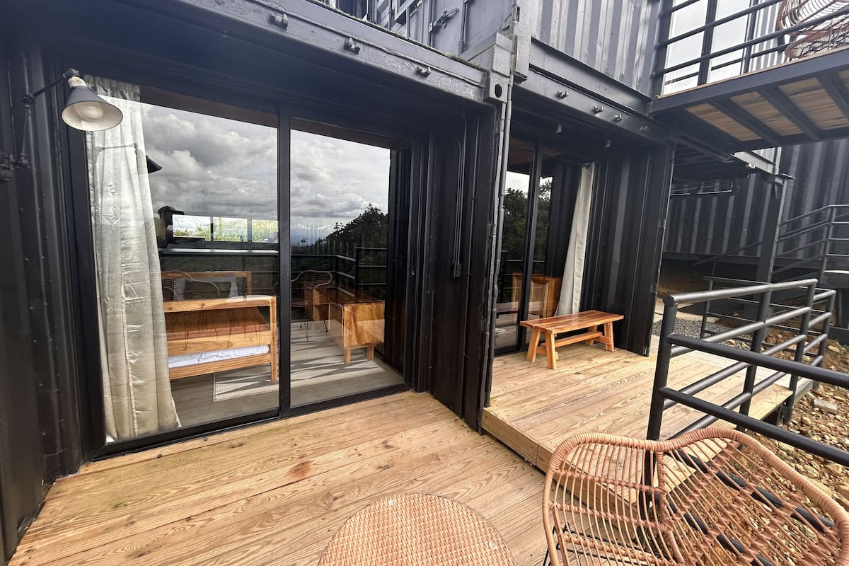 Une terrasse extérieure moderne, dotée de meubles en bois, d’un fauteuil en osier et d’une rambarde en métal.
