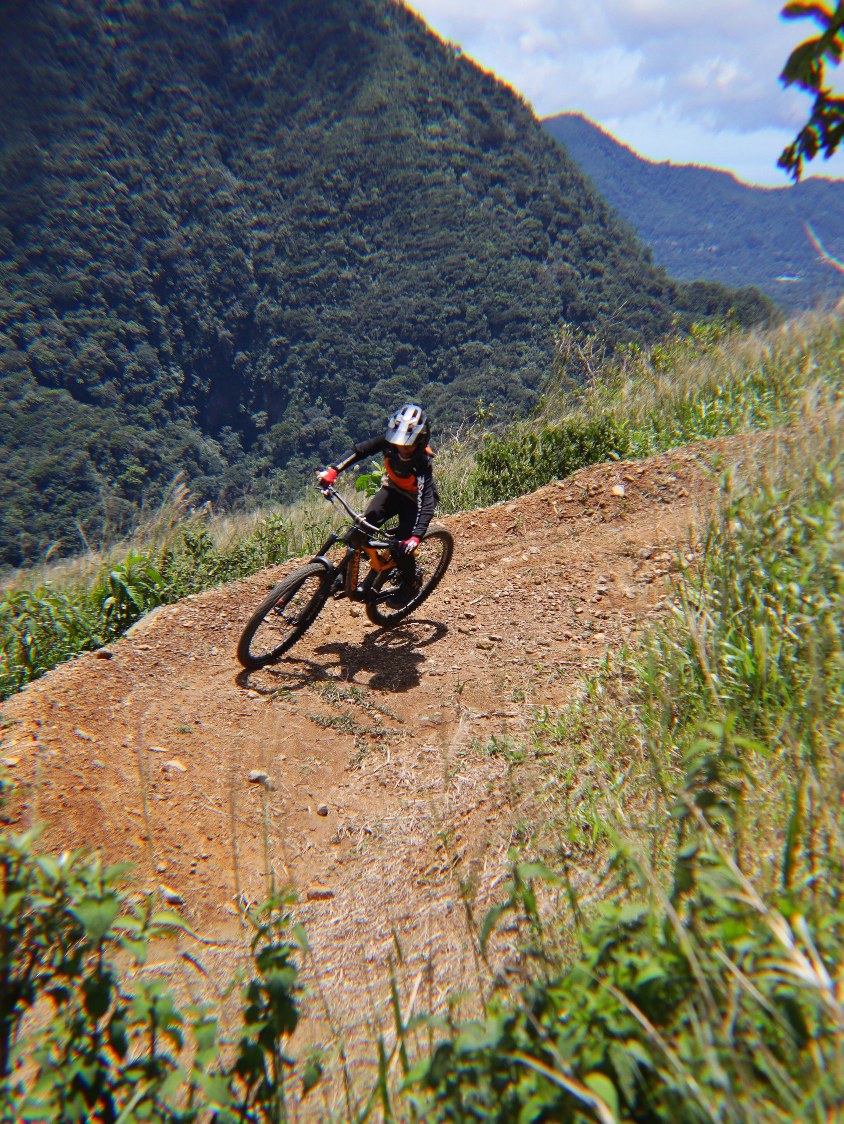 A mountain biker on a dirt trail with a forested mountain in the background.