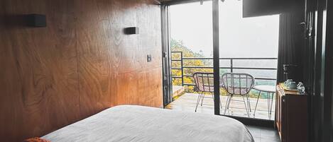 Un dormitorio con una cama grande, paredes de madera, un balcón con una silla y vistas al exterior.