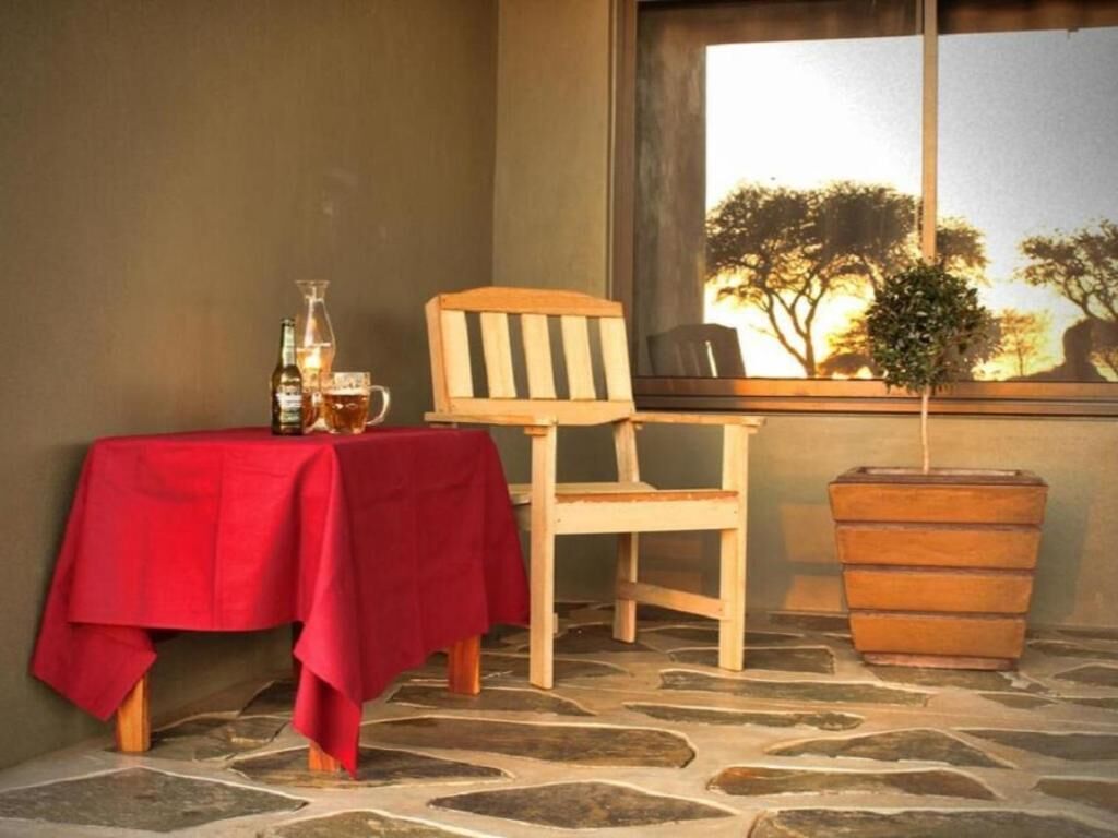 Um canto com uma mesa vermelha, uma cadeira de madeira, um vaso com planta e um barril de madeira.