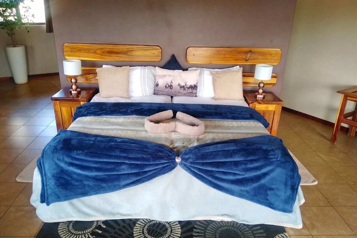 Een net opgemaakt bed met een blauw-witte spreideken, twee houten nachtkastjes met lampen en een kamerkleed op de vloer.