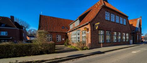 A traditional brick building with a steeply pitched roof, large windows, and a visible chimney.