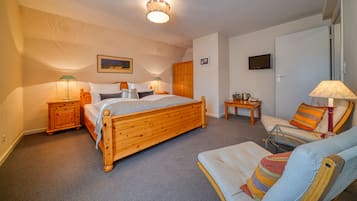 A bedroom with a wooden bed, two bedside tables with lamps, a chair, a small table, and a television on the wall.