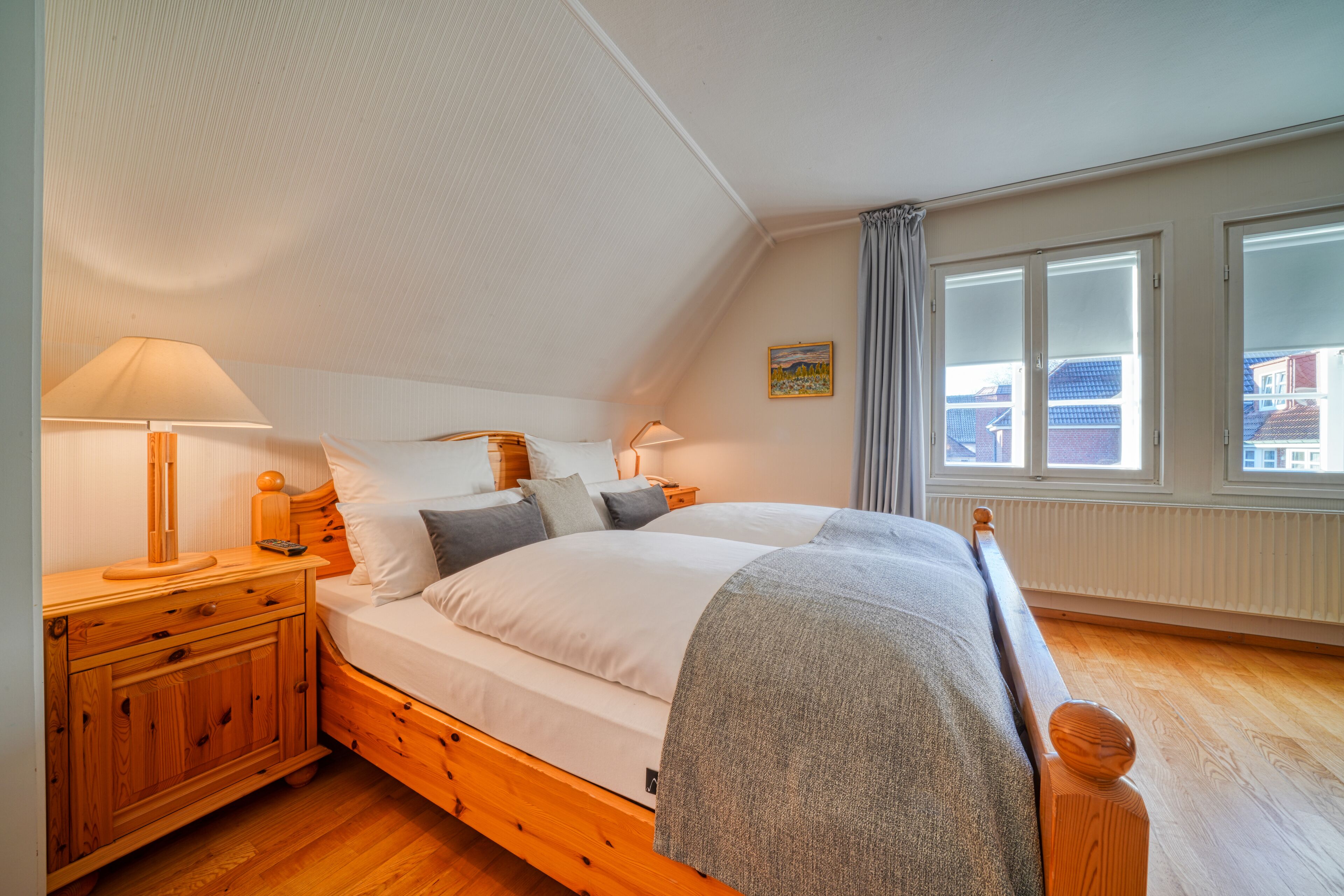 A bedroom with a wooden bed, two bedside tables, a lamp, and a window with curtains.