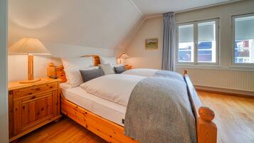 A bedroom with a wooden bed, two bedside tables, a lamp, and a window with curtains.