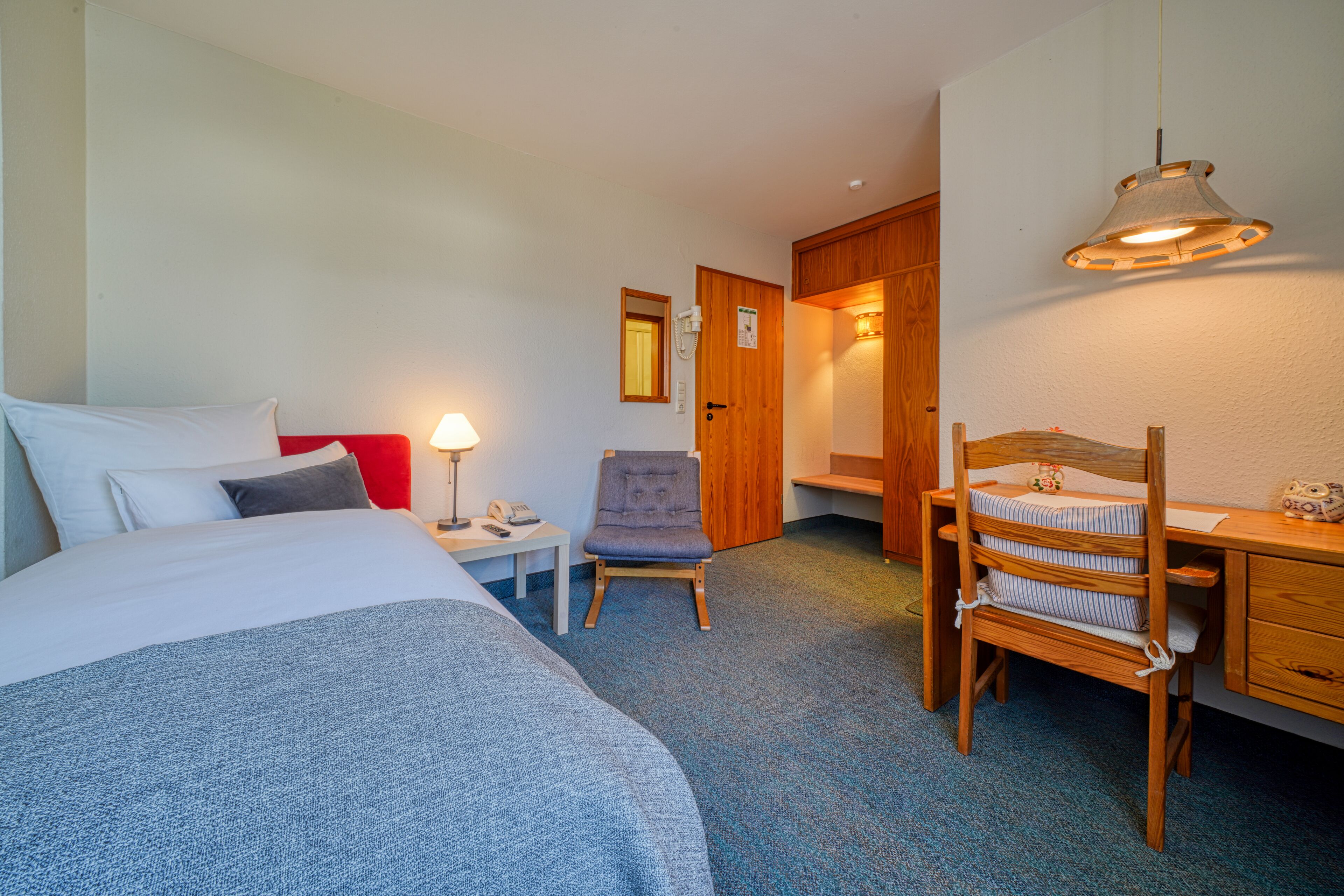Una habitación de hotel con una cama, un escritorio, una silla, una lámpara y una puerta.