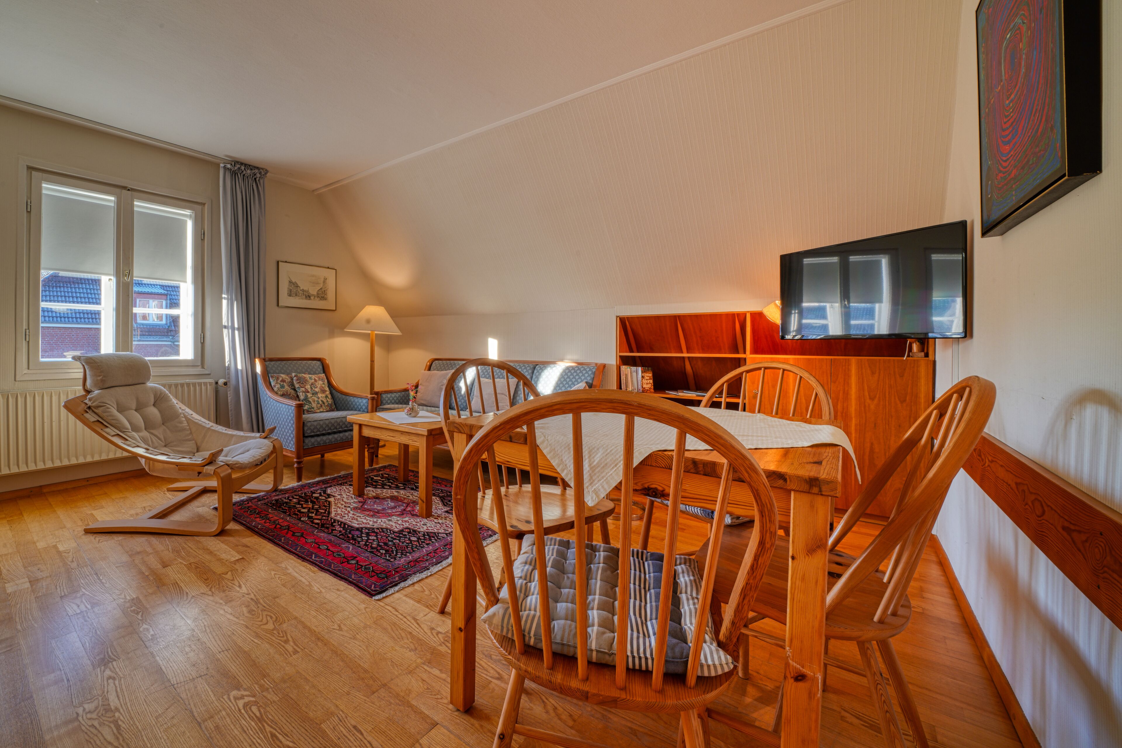 Ein gemütliches Wohnzimmer mit einem Holzesstisch, Stühlen, einer Couch und einem Fernseher.