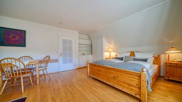 Ein Schlafzimmer mit einem hölzernen Bett, einem Esstisch mit Stühlen, einer weißen Tür und einem Gemälde an der Wand.