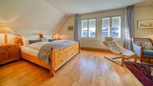 Un dormitorio con cama de madera, una mecedora, una ventana con cortinas y un radiador.