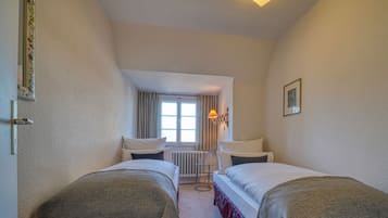 Une chambre d’hôtel avec deux lits simples, une petite table, une chaise, un radiateur et une fenêtre avec des rideaux.