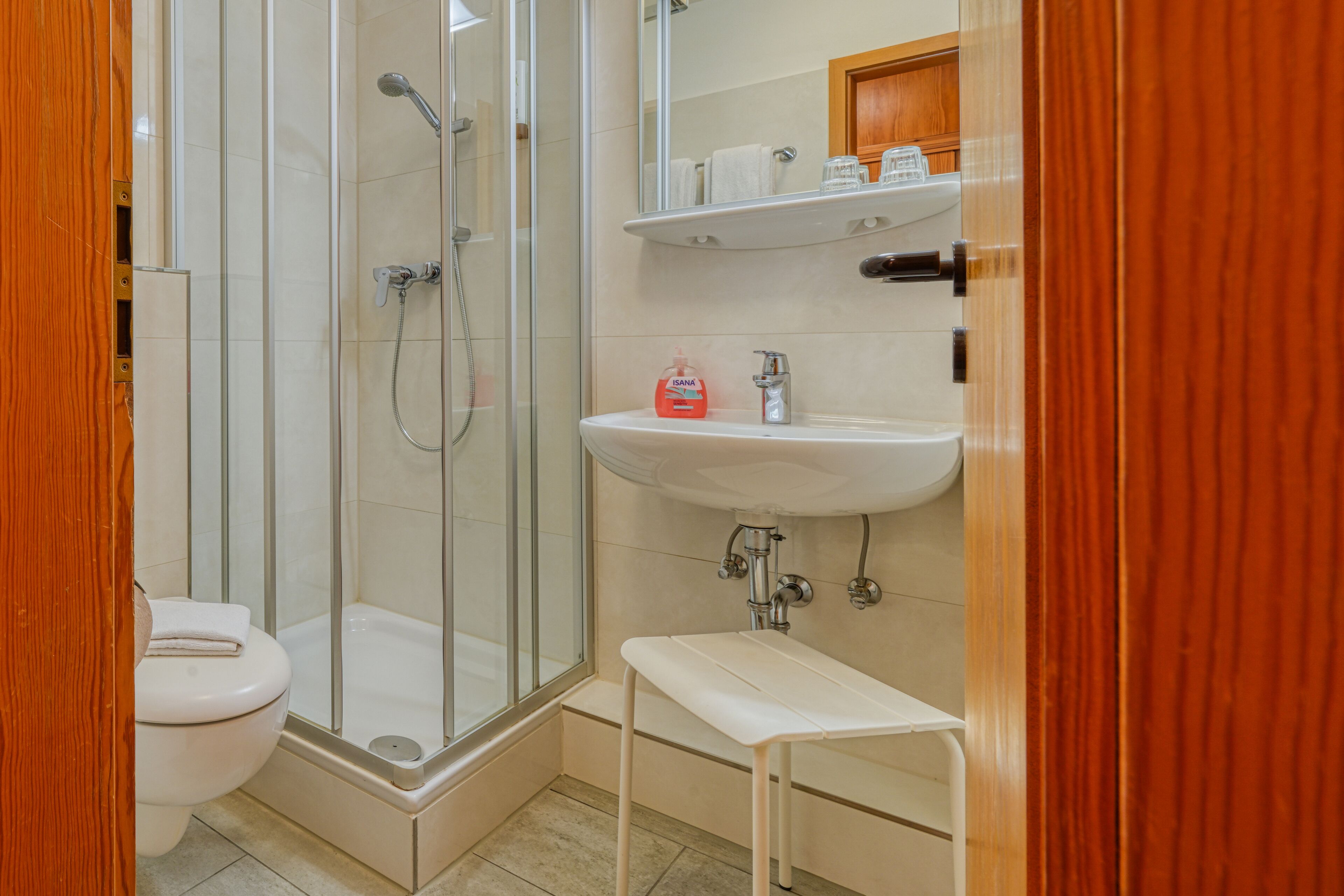 A bathroom with a glass-enclosed shower, a white sink, and a wooden door.