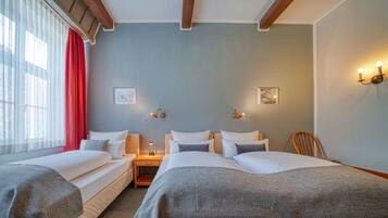 A hotel room with two beds, a nightstand, a chair, and a window with curtains.