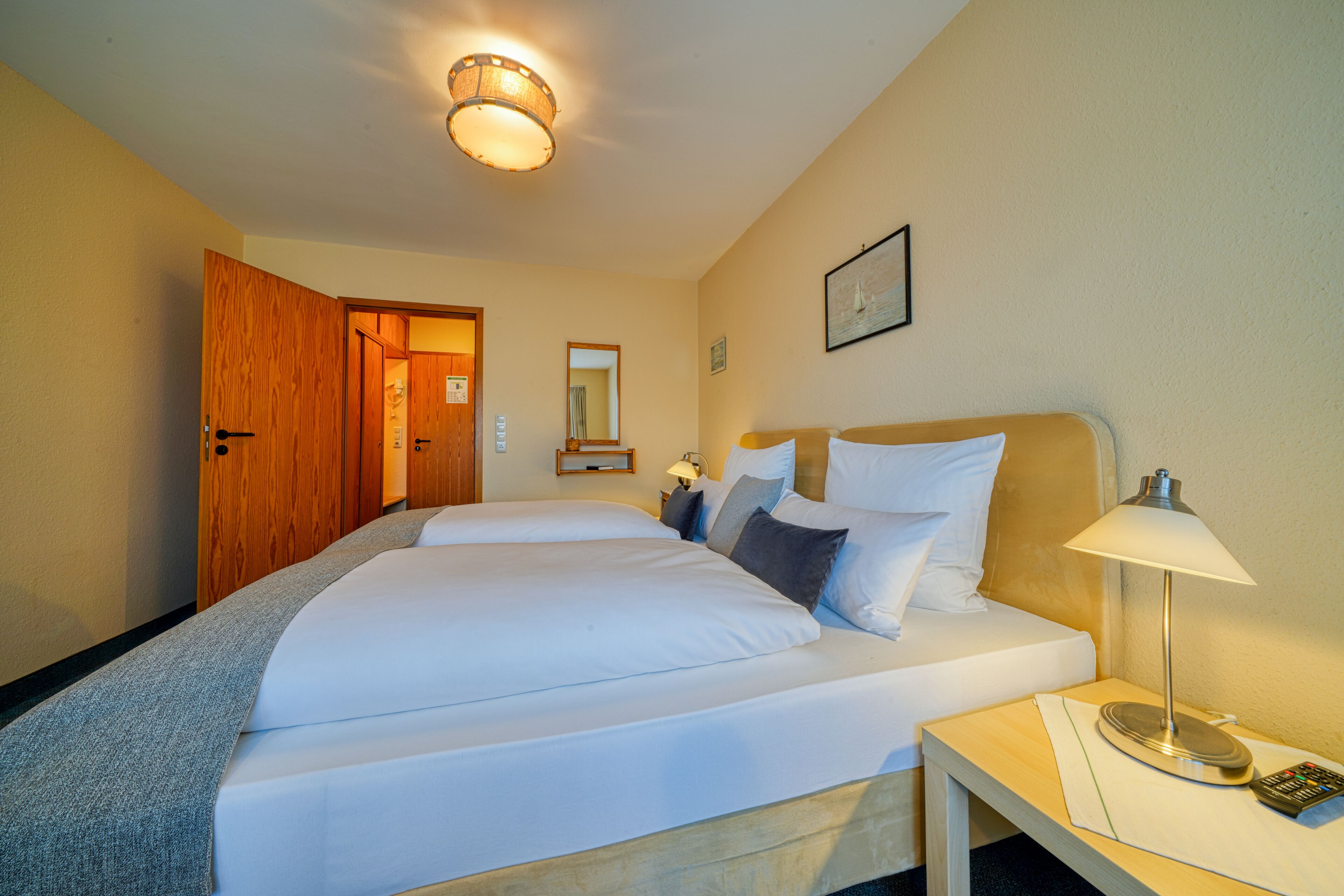 Et hotelværelse med to senge, et natbord med lampe, et spejl og en dør til et andet rum.