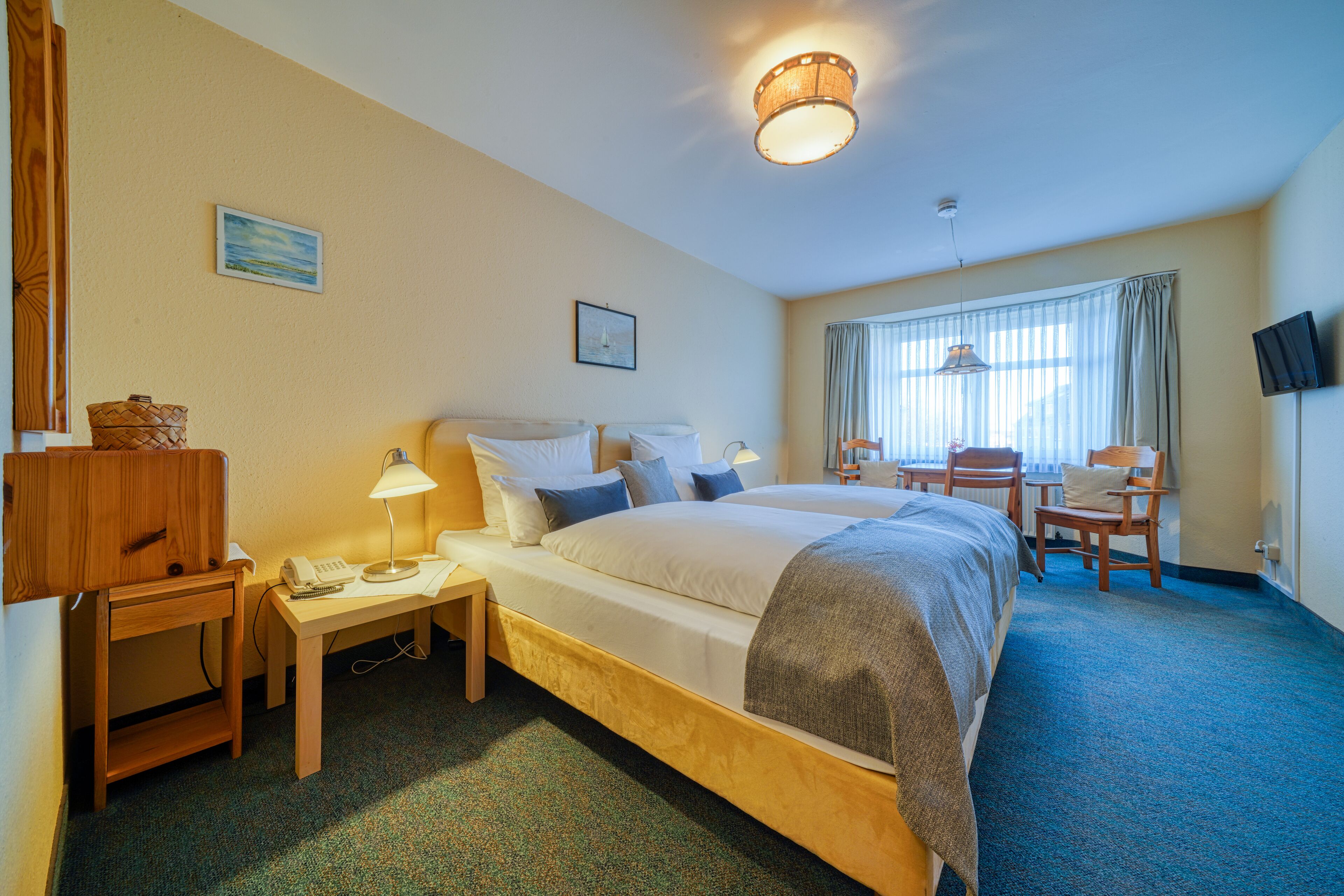 A hotel room with a bed, bedside tables, a desk, a chair, and a television.