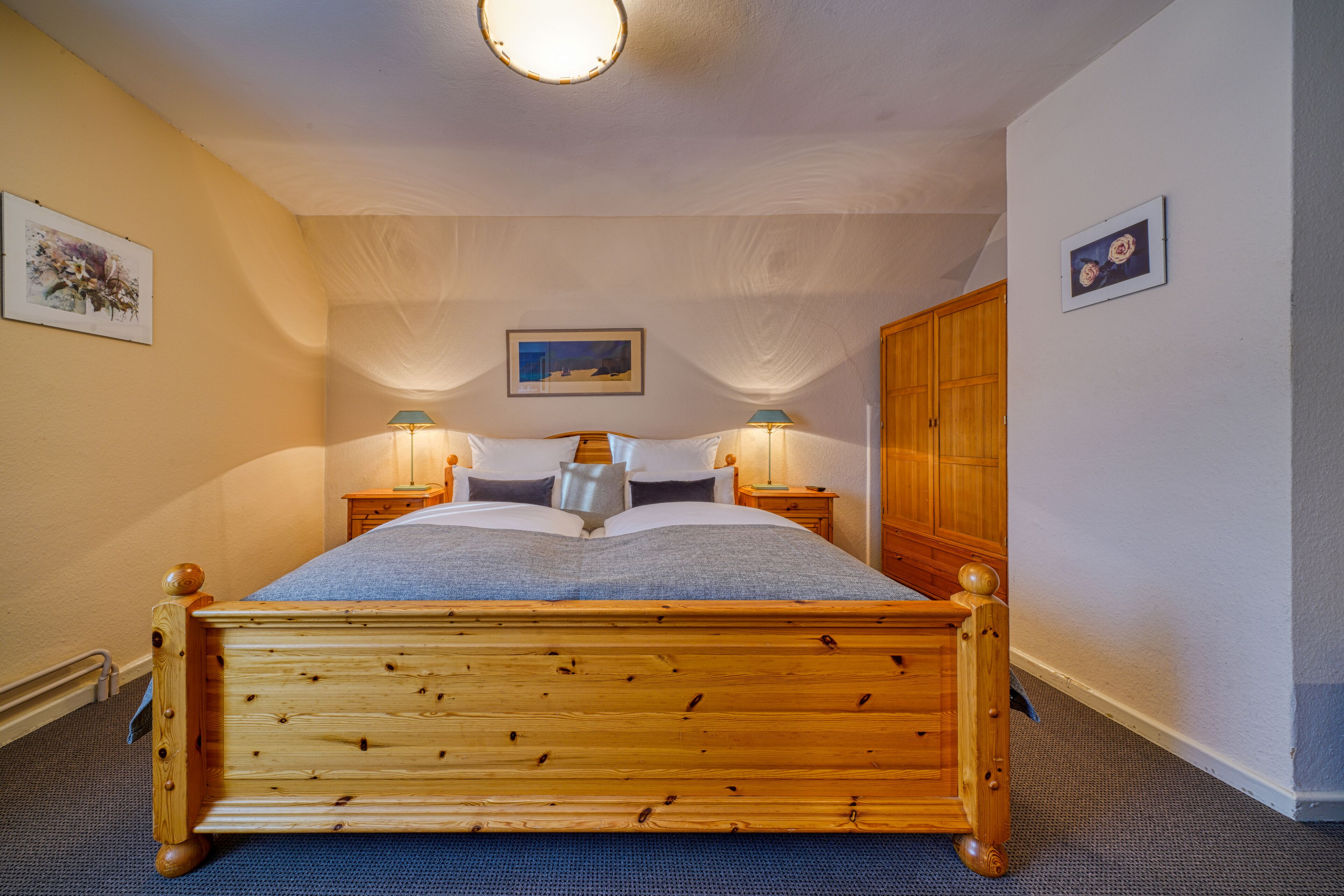 Uma cama de madeira com dossel, com colcha azul, duas luminárias de cabeceira e um quadro na parede.
