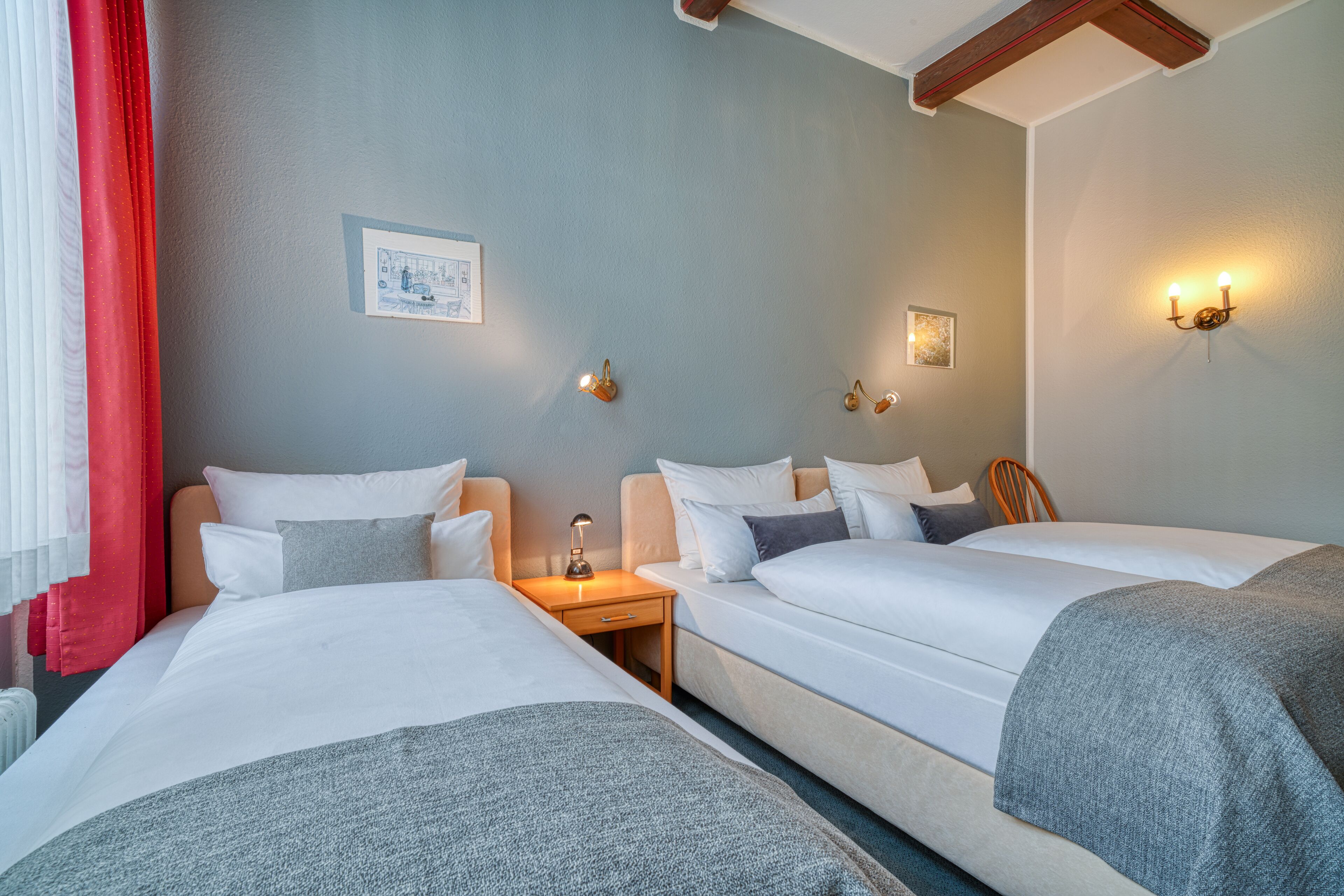 Habitación de hotel con dos camas, una mesita de noche con lámpara, y lámparas fijadas a la pared.